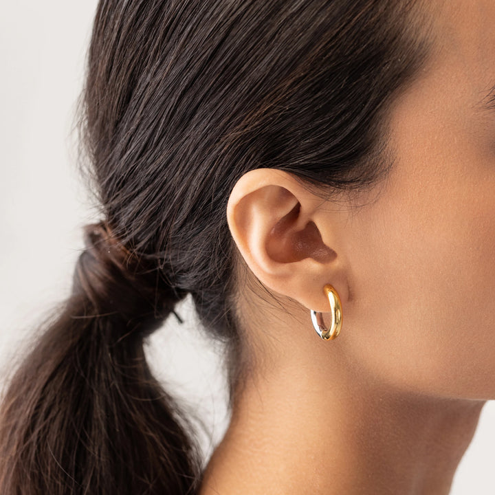 Model wearing the Slim Mix Huggies, a chic pair of two-tone hoop earrings features a combination of gold and silver tones.