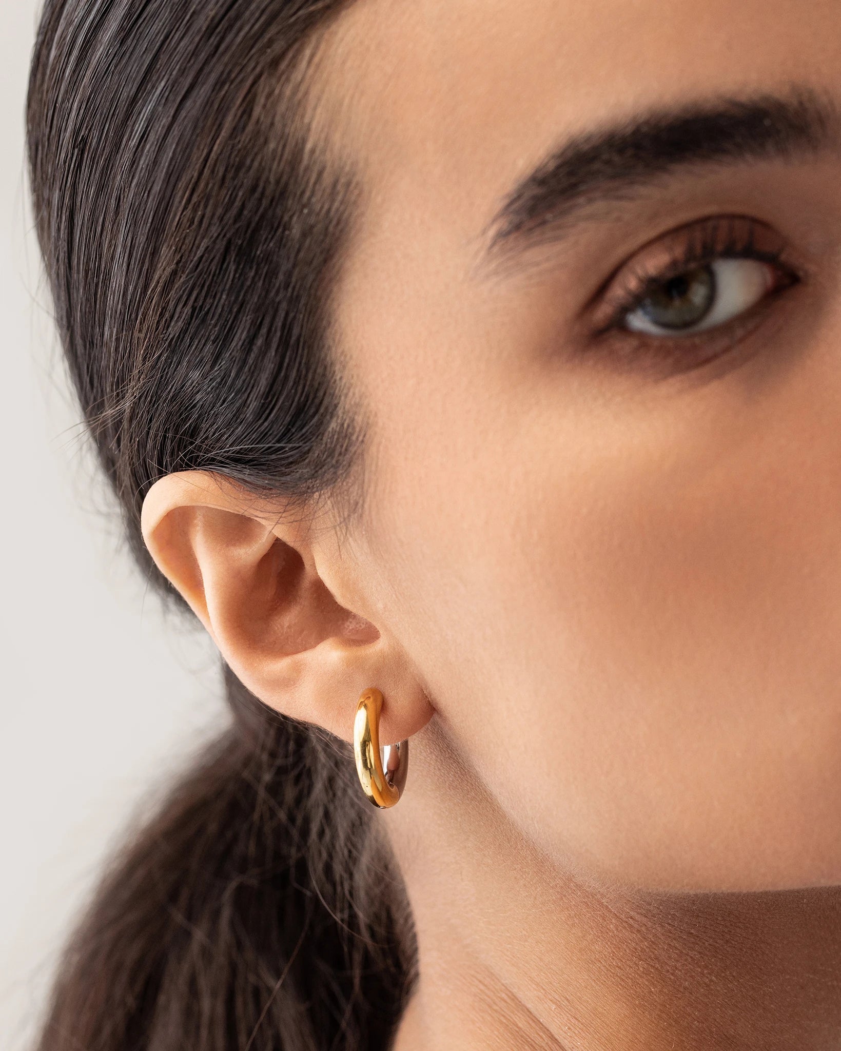 Model wearing the Slim Mix Huggies, a chic pair of two-tone hoop earrings features a combination of gold and silver tones.