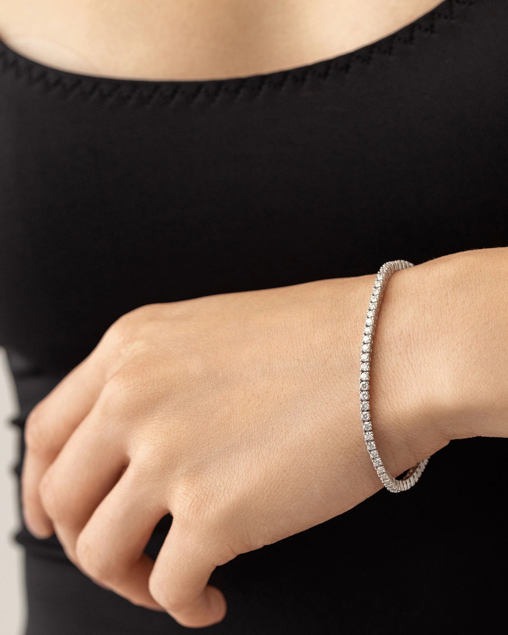 The Sparkling Thin Tennis Bracelet, which is a single silver bracelet featuring a delicate row of shimmering stones, elegantly worn on the wrist, showcasing its timeless and minimalist design ideal for everyday elegance.