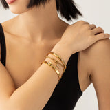 Model wearing the ARROWHEAD BRACELET STACK, a stylish gold bangle set featuring 3 bracelets with intricate arrowhead details and sparkling diamonds. Includes a chain bracelet with arrowhead and triangle charms. 