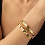 Model wearing the ARROWHEAD BRACELET STACK, a stylish gold bangle set featuring 3 bracelets with intricate arrowhead details and sparkling diamonds. Includes a chain bracelet with arrowhead and triangle charms. 