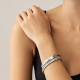 Model wearing the Silver Gear Bracelet Stack, a five piece silver bracelet stack includes three unique bangle styles, one featuring a row of sparkling stones and another with a sleek, minimalist design. Two delicate tennis bracelets with shimmering stones.