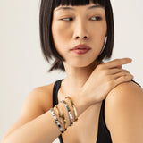 Model wearing the Spiked Armor Bracelet Stack, a four-piece gold and silver bracelet stack featuring bangles with spike accents, diamond-like stones.