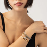 Model wearing the Mix Gear Bracelet Stack, a four-piece gold and silver bracelet stack featuring two bangles and two chains with a variety of charms, including a teardrop charm, a spike charm, and a disc charm accented with diamond-like stones.