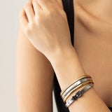 Model wearing The BELTED BRACELET STACK, a stylish four-piece bangle set featuring a mix of gold and silver tones with intricate details like a buckle clasp and diamond accents. 