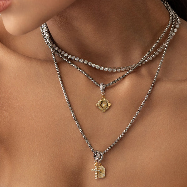 Model wearing a bubble tennis necklace and two silver chains with 3 clip on charms including The Go North Clip On Charm, a gold compass charm accented with diamond-like stones. and the cross and celestial star charms.