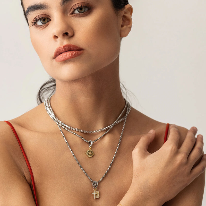 Model wearing a bubble tennis necklace and two silver chains with 3 clip on charms including The Go North Clip On Charm, a gold compass charm accented with diamond-like stones. and the cross and celestial star charms.