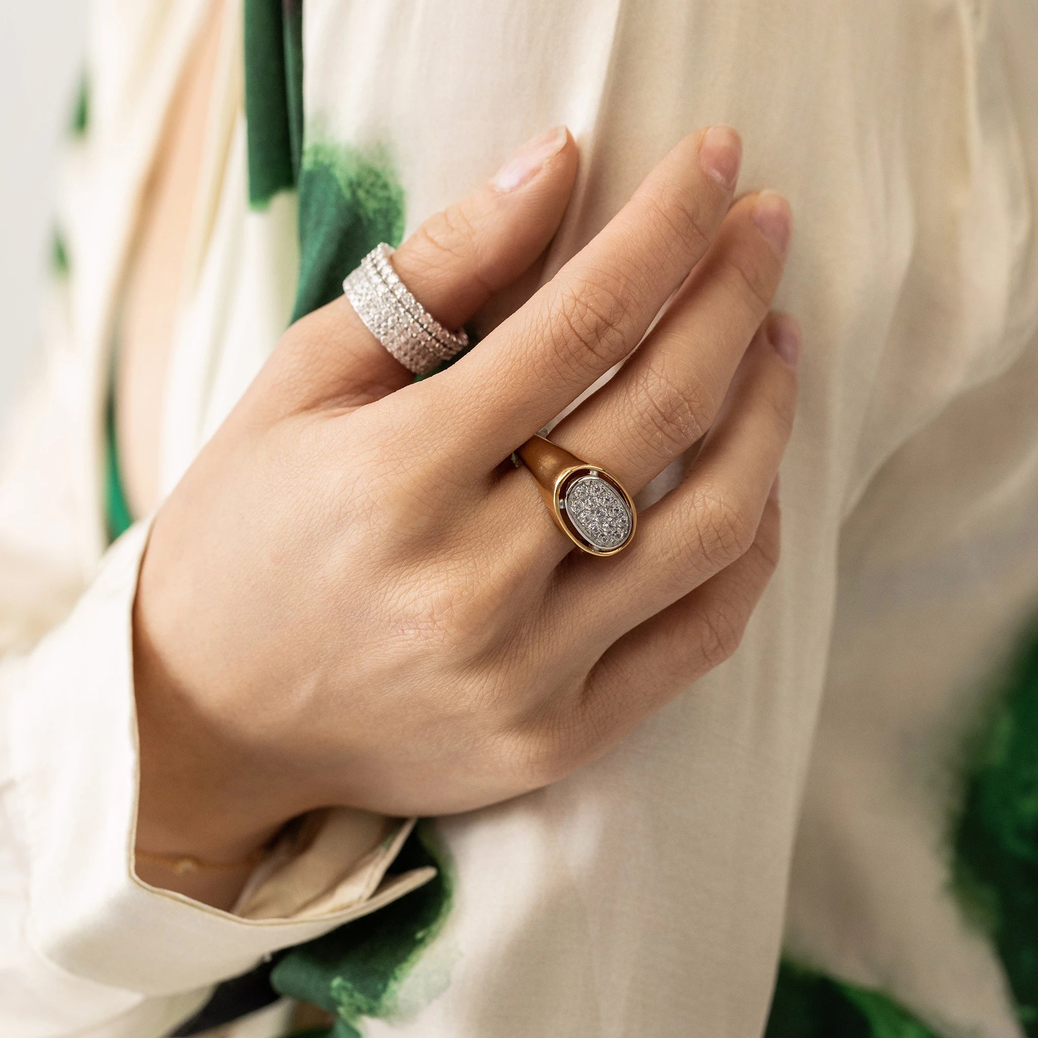Model wearing two diamond rings on her thumb and the BOLD GLIMMER RING, a striking gold ring featuring a large oval-shaped setting adorned with sparkling diamonds on her middle finger. 