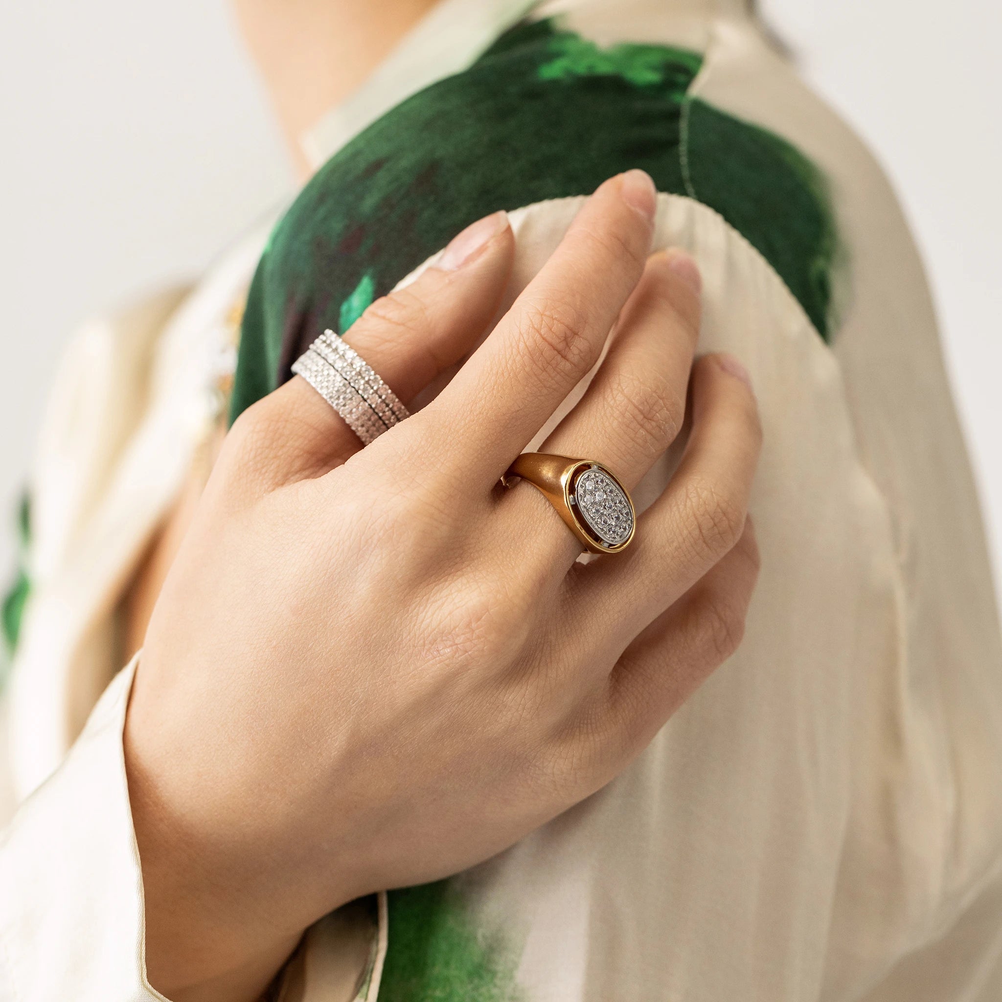 Model wearing two diamond rings on her thumb and the BOLD GLIMMER RING, a striking gold ring featuring a large oval-shaped setting adorned with sparkling diamonds on her middle finger. 