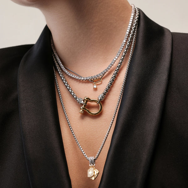 The Herradura Signature Charmed Tennis Set, which is a three-piece layered silver necklace set, features intricate tennis chains with shimmering stones and gold accents, including a bold clasp and two elegant gold charms for a statement-making yet refined style.