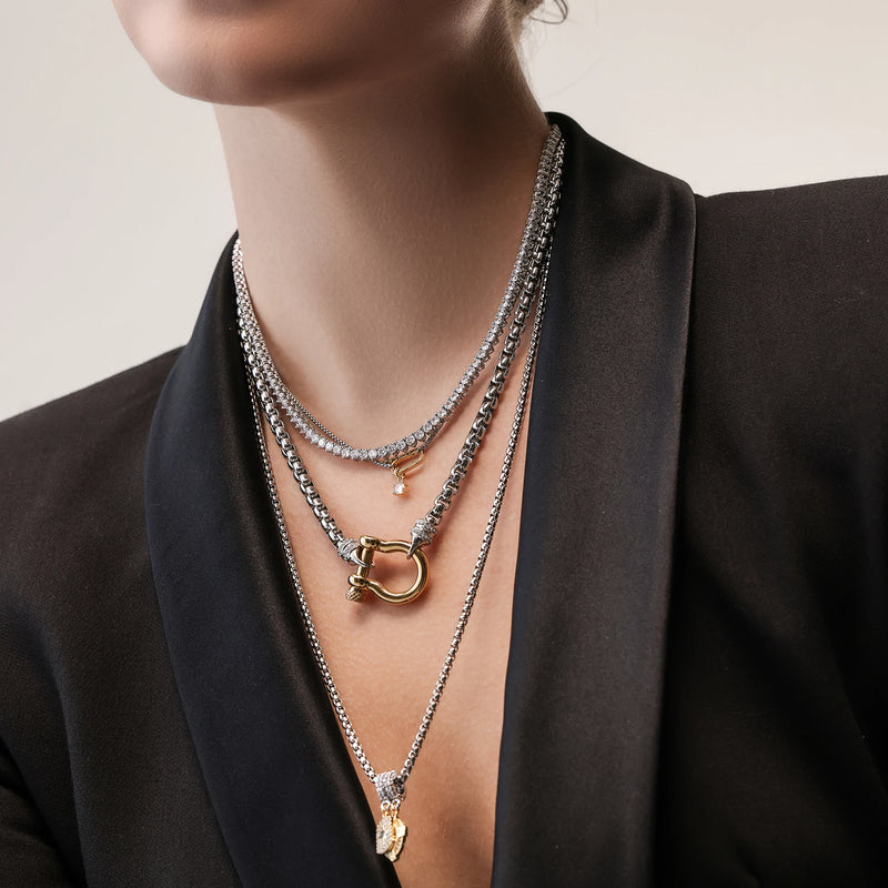 The Herradura Signature Charmed Tennis Set, which is a three-piece layered silver necklace set, features intricate tennis chains with shimmering stones and gold accents, including a bold clasp and two elegant gold charms for a statement-making yet refined style.