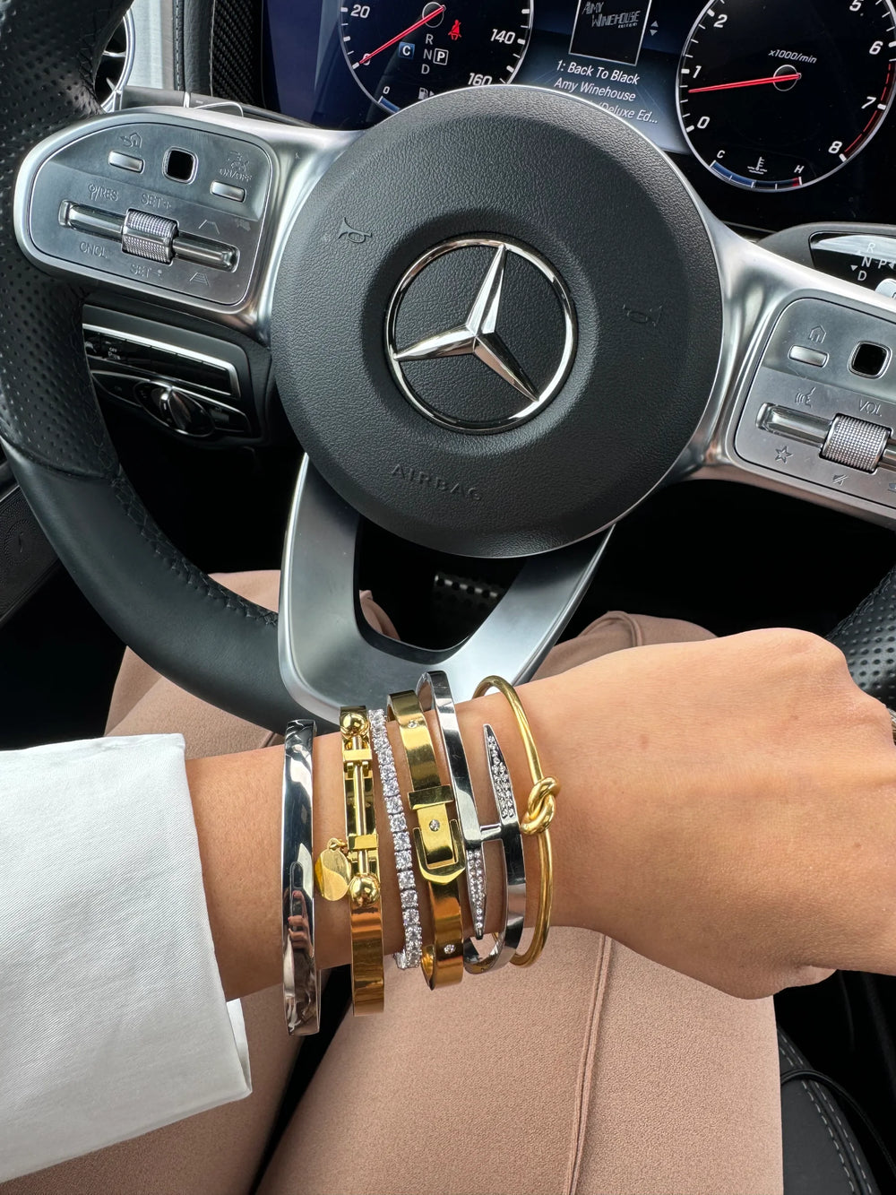 bracelet stack displayed on woman's wrist paired with gold and silver bracelets from Artizan Joyeria posed in front of a Mercedez Benz steering wheel