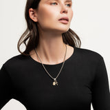 The Double the Charm Necklace, which is a single silver-toned chain necklace featuring two distinct charm pendants—a lock and a cross—styled for a bold, modern look. |||