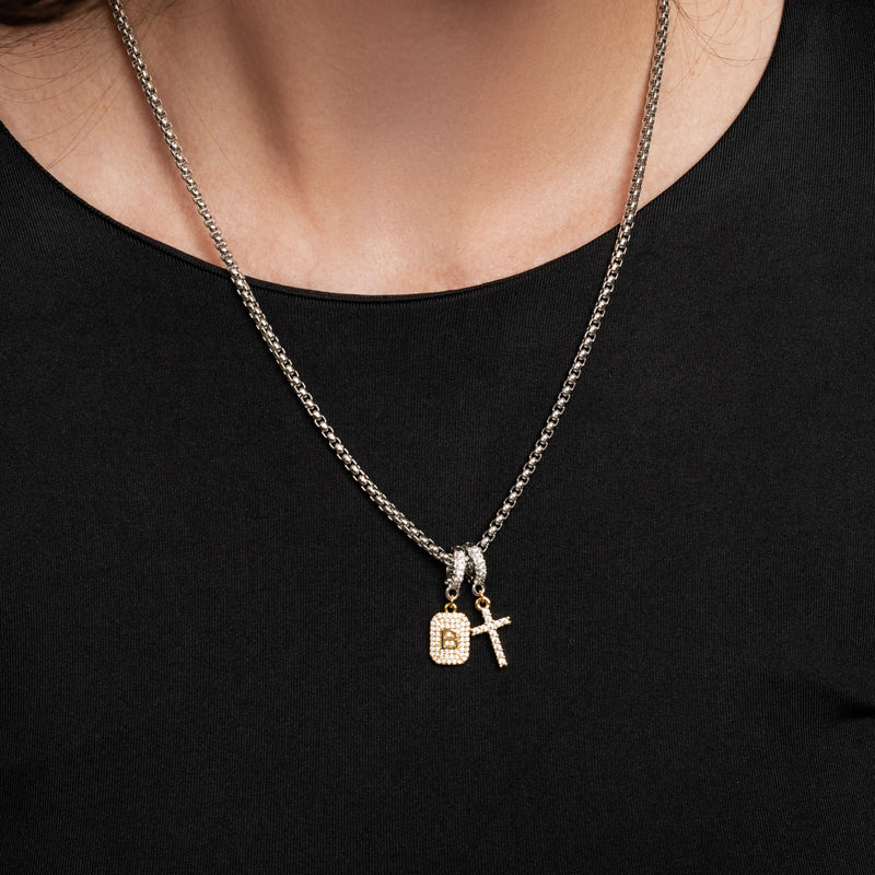 The Double the Charm Necklace, which is a single silver-toned chain necklace featuring two distinct charm pendants—a lock and a cross—styled for a bold, modern look. 
