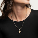 The Double the Charm Necklace, which is a single silver-toned chain necklace featuring two distinct charm pendants—a lock and a cross—styled for a bold, modern look. |||