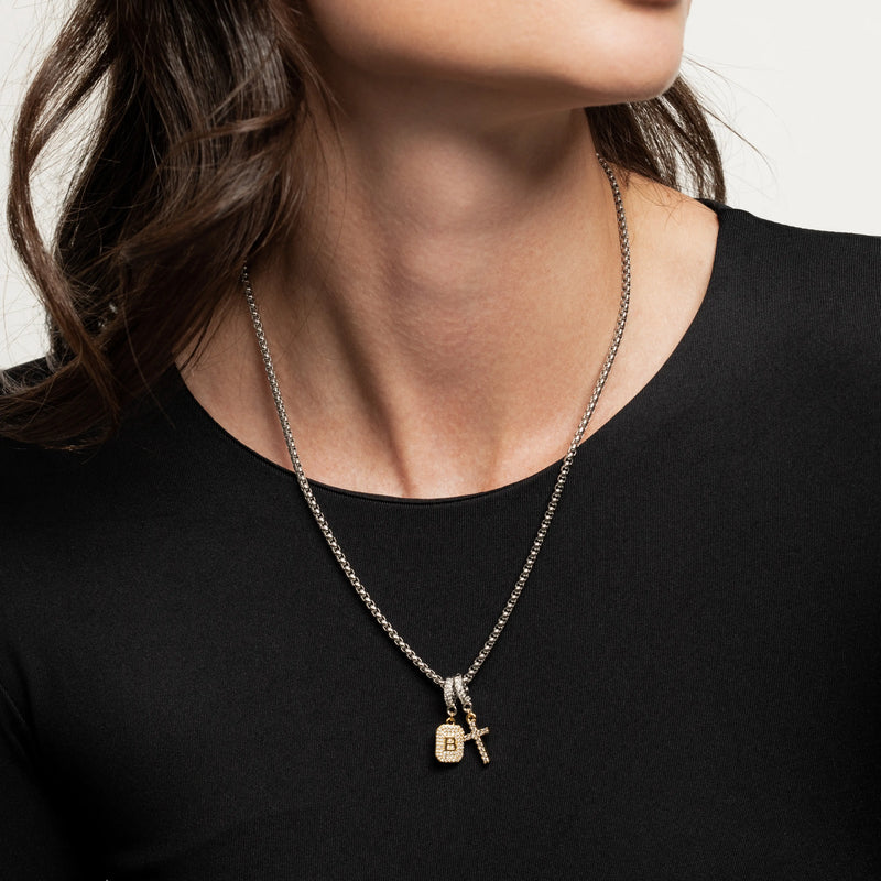 The Double the Charm Necklace, which is a single silver-toned chain necklace featuring two distinct charm pendants—a lock and a cross—styled for a bold, modern look. 