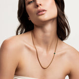 The Emerald Point Necklace, which is a delicate gold chain necklace featuring a single emerald stone, worn by a woman in a strapless top. ||| GOLD