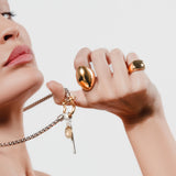 Close-up of woman wearing two gold rings, including the Fierce Ring Gold, and holding a silver and gold charm necklace with pendants. ||| GOLD
