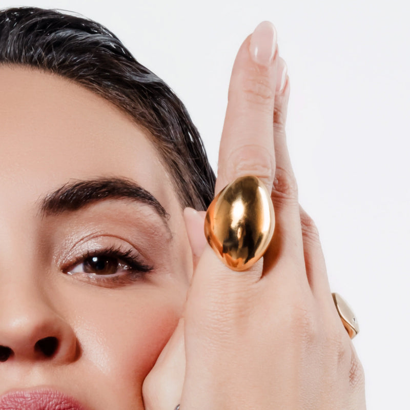 Close-up of woman wearing two gold rings, including the bold Fierce Ring Gold on index finger and a smooth band ring on pinky. 