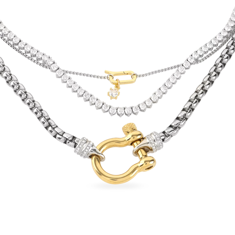 The Herradura Signature Charmed Tennis Set, which is a three-piece layered silver necklace set, features intricate tennis chains with shimmering stones and gold accents, including a bold clasp and two elegant gold charms for a statement-making yet refined style.