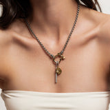 The Herradura Signature Double Take Gold, which is a mixed metal necklace featuring a gold and silver chain with a toggle clasp, adorned with a golden charm and a small key pendant, worn by a woman in a strapless top. ||| GOLD