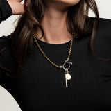 The Double the Charm Necklace, which is a single silver-toned chain necklace featuring two distinct charm pendants—a lock and a cross—styled for a bold, modern look. ||| SILVER