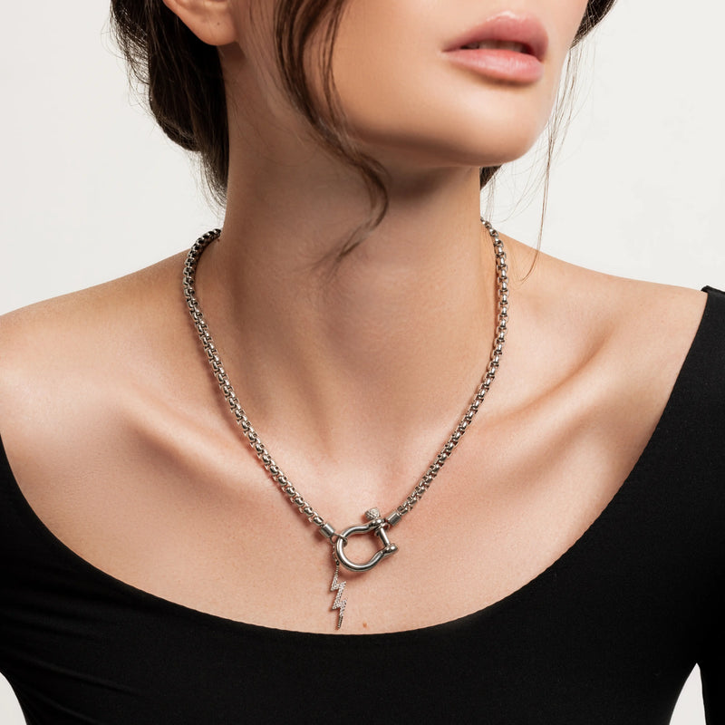 The Herradura Thunder Silver, which is a bold silver chain necklace featuring a toggle clasp with a lightning bolt pendant, worn by a woman in a black off-shoulder top.