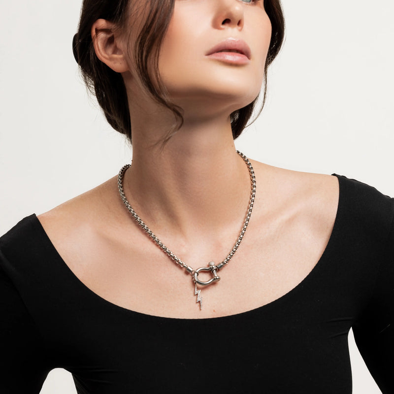 The Herradura Thunder Silver, which is a bold silver chain necklace featuring a toggle clasp with a lightning bolt pendant, worn by a woman in a black off-shoulder top.