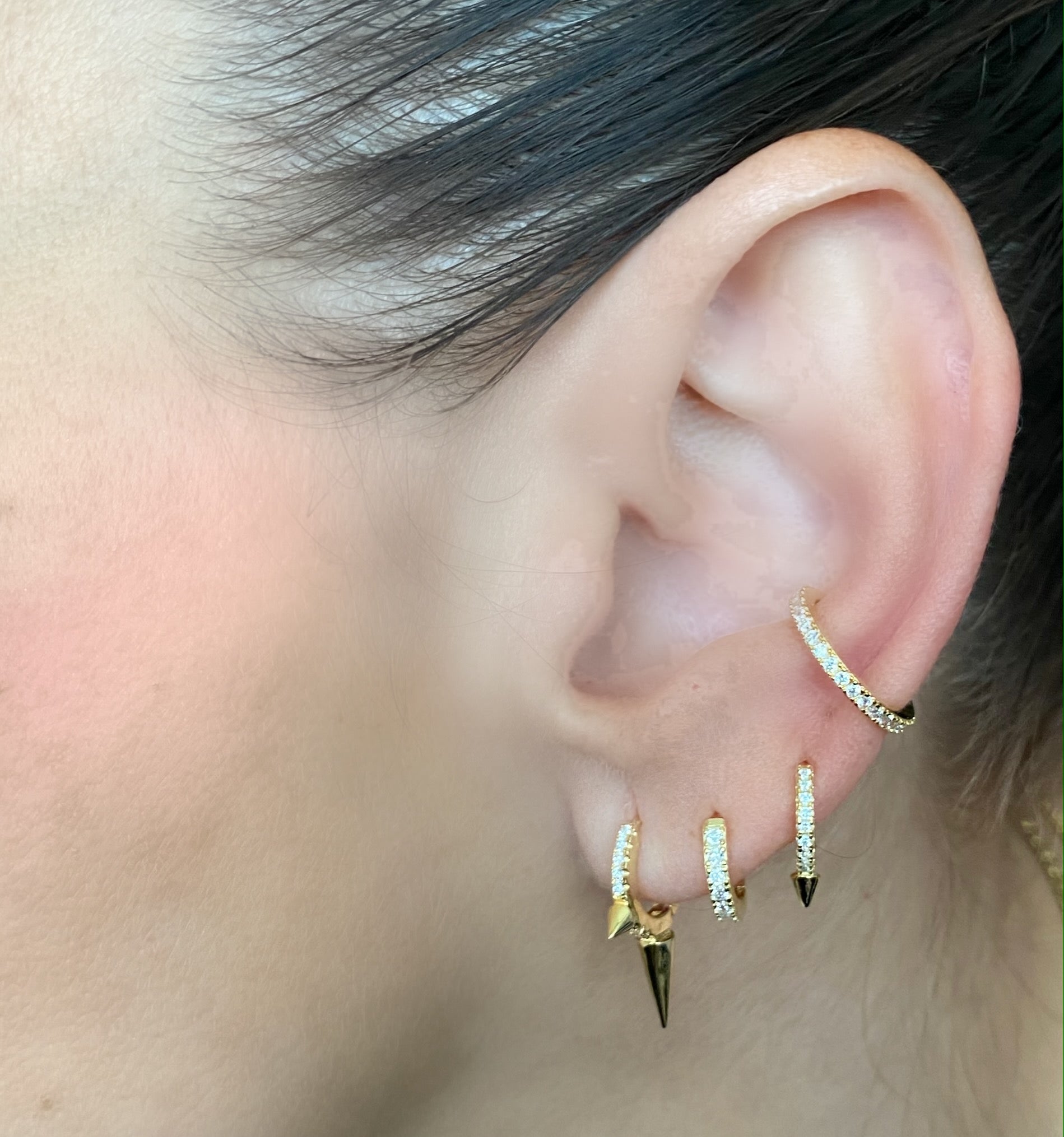 Model wearing the Clear Ear cuff gold that has cubic zirconia stones and 3 more small loop earrings whith spikes and cubic zirconia stones as well. ||| GOLD