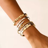 Model wearing the Khanti Bracelet Stack, a five-piece gold and silver bracelet stack featuring bangles with a variety of  accents, including a knotted bangle, a buckle bangle with diamond-like stones, a bar bangle, and a bangle with diamond-like stones and a heart charm.