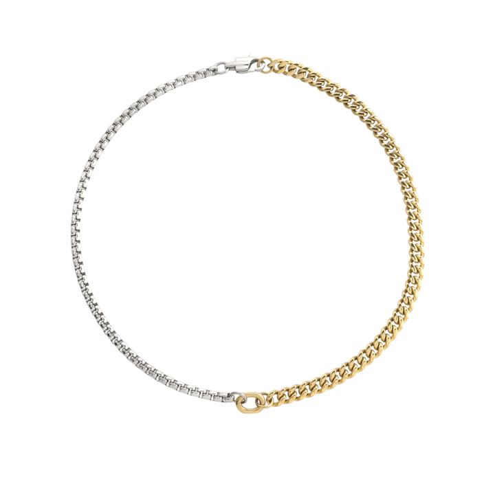 Close-up of OPPOSITES ATTRACT CHAIN NECKLACE, two-tone chain with silver box links on one side and gold Cuban links on the other, joined at the center with a gold oval connector. |||  MIX