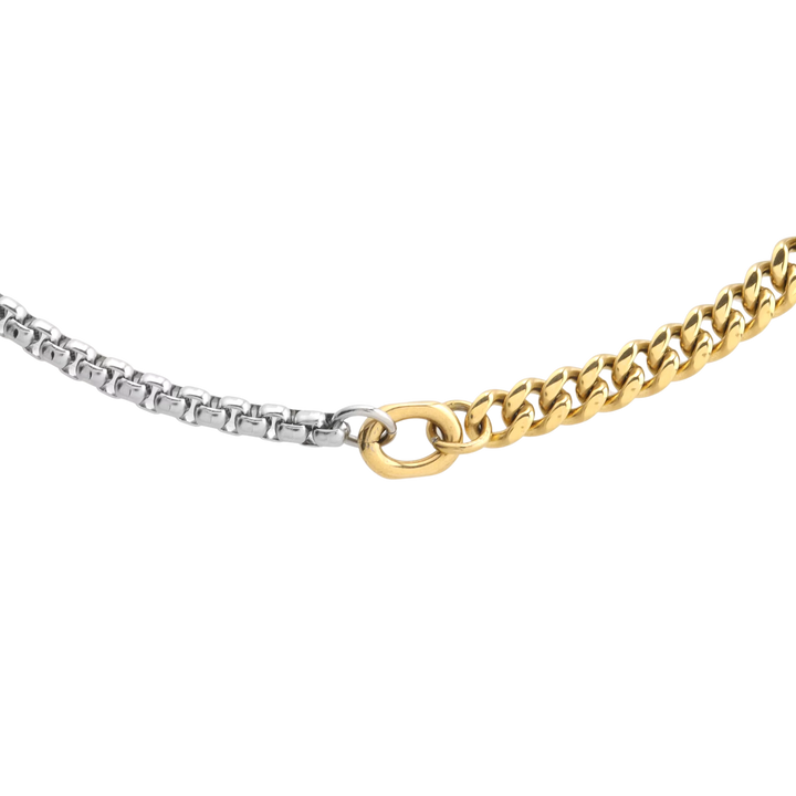 Close-up of OPPOSITES ATTRACT CHAIN NECKLACE, two-tone chain with silver box links on one side and gold Cuban links on the other, joined at the center with a gold oval connector. |||  MIX