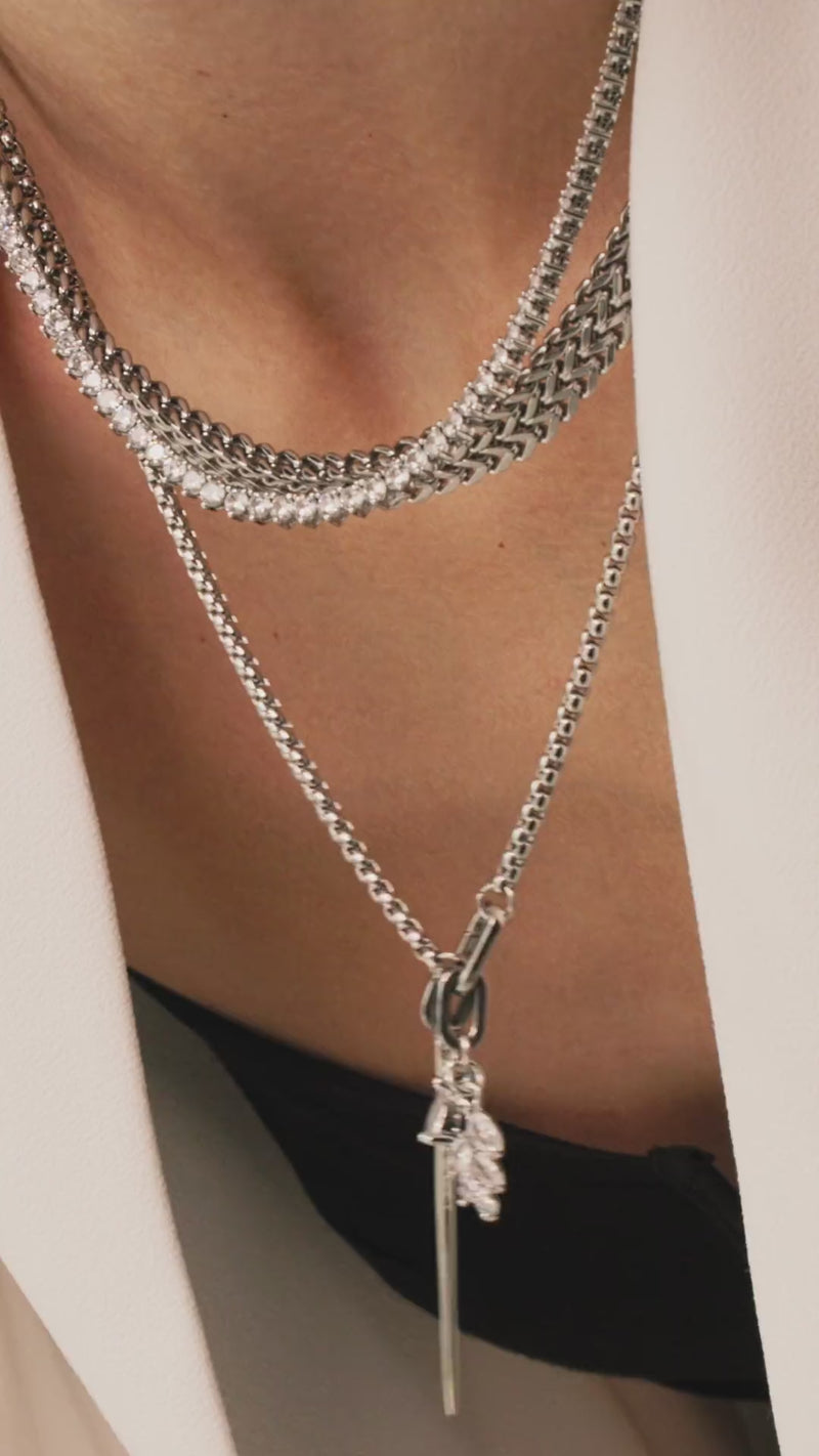 Model wearing The Needle and the Tennis Necklace Set, a three-piece silver necklace set featuring two chains, a diamond-like tennis necklace, and a dangling spike charm.