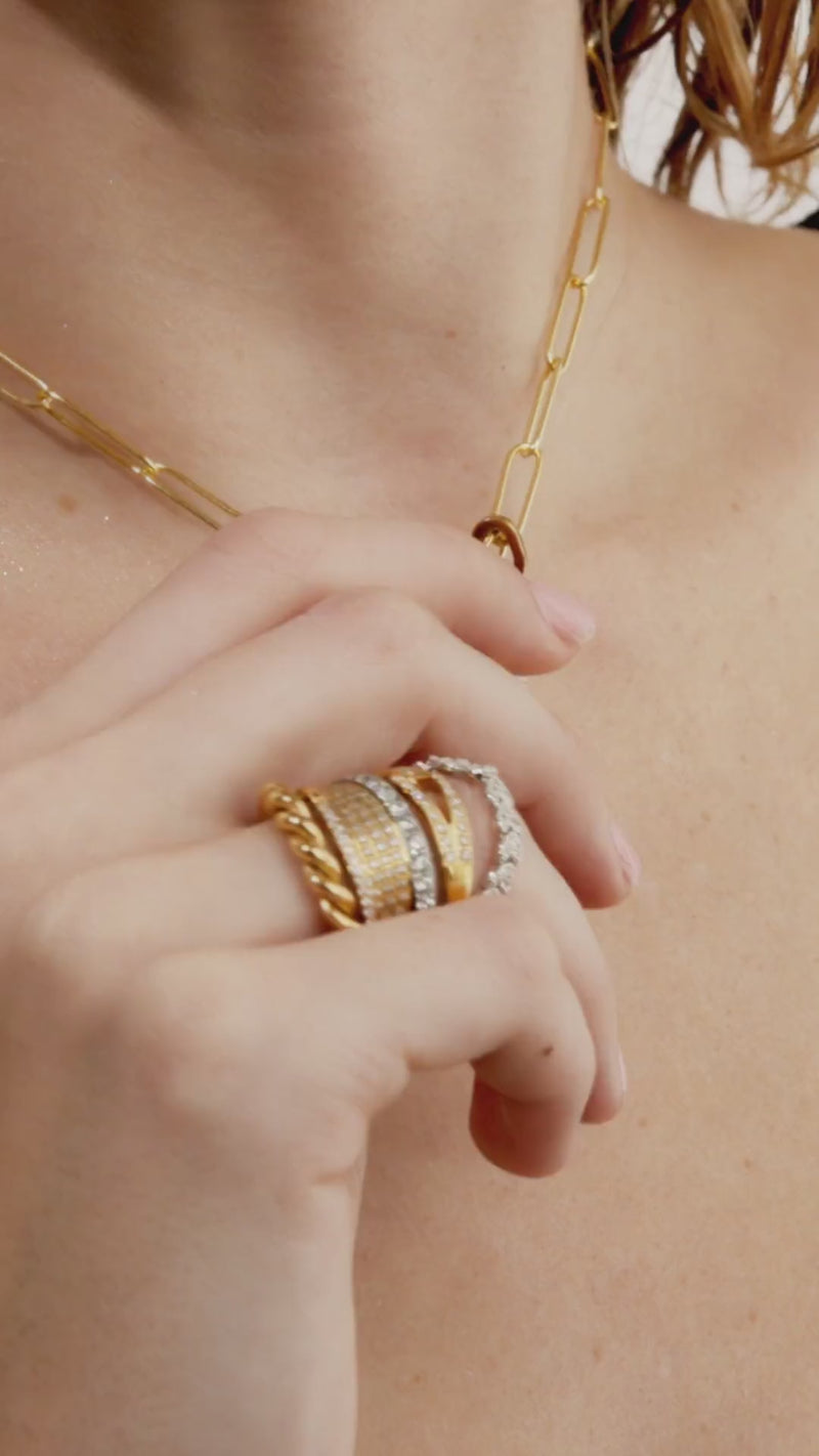 Video of a model wearing The Paper Clip Chain, a gold chain necklace featuring elongated, open oval links reminiscent of paperclips and also various artizan rings.