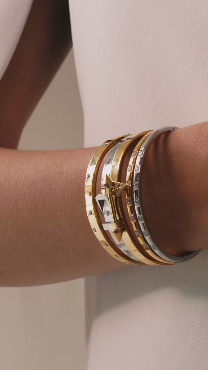 Video of a model wearing the Triangle Stack, a five-piece bangle set featuring gold and silver bangles with cubic zirconia accents and a triangle clasp detail.