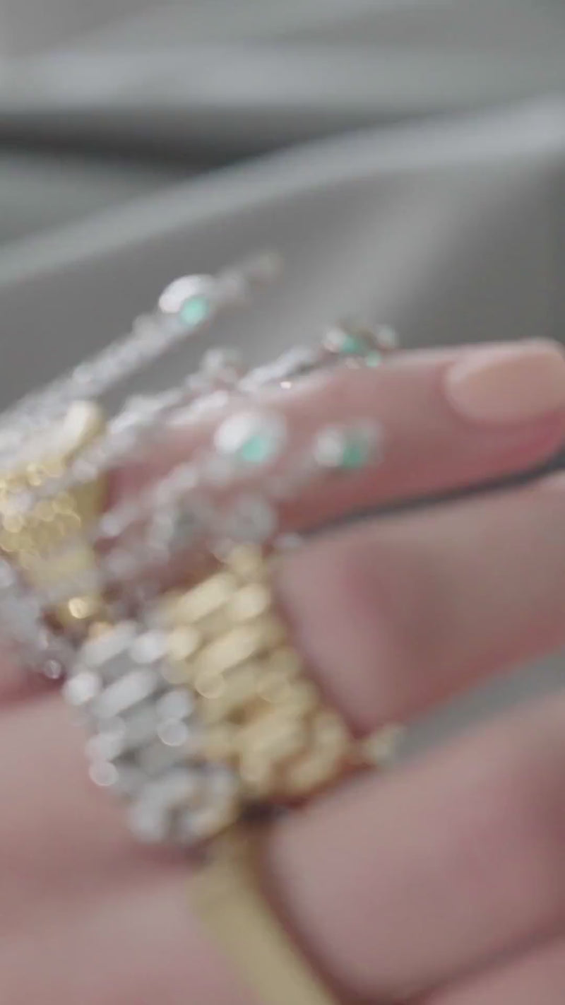 Video of a model wearing multiple artizan rings bracelets and necklaces featuring the Emerald Waterfall Ring, a silver ring featuring cascading chains with emerald and diamond-like accents.
