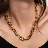 The Puerto Chain Necklace Gold, which is a bold gold chain necklace featuring large, rectangular links, worn by a woman in a black top. ||| GOLD