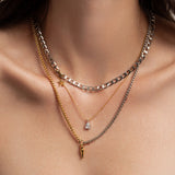 The Shini Spike Trio Necklace Set, a set of three layered necklaces in mixed gold and silver tones, featuring a combination of delicate chains, a crystal charm, and a bold spike pendant, worn by a model.