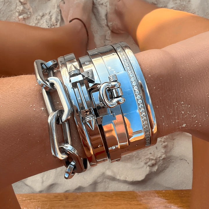 SILVER CORE BRACELET STACK featuring multiple bold designs, including a chunky chain and Herradura bangle, worn on a sandy beach.