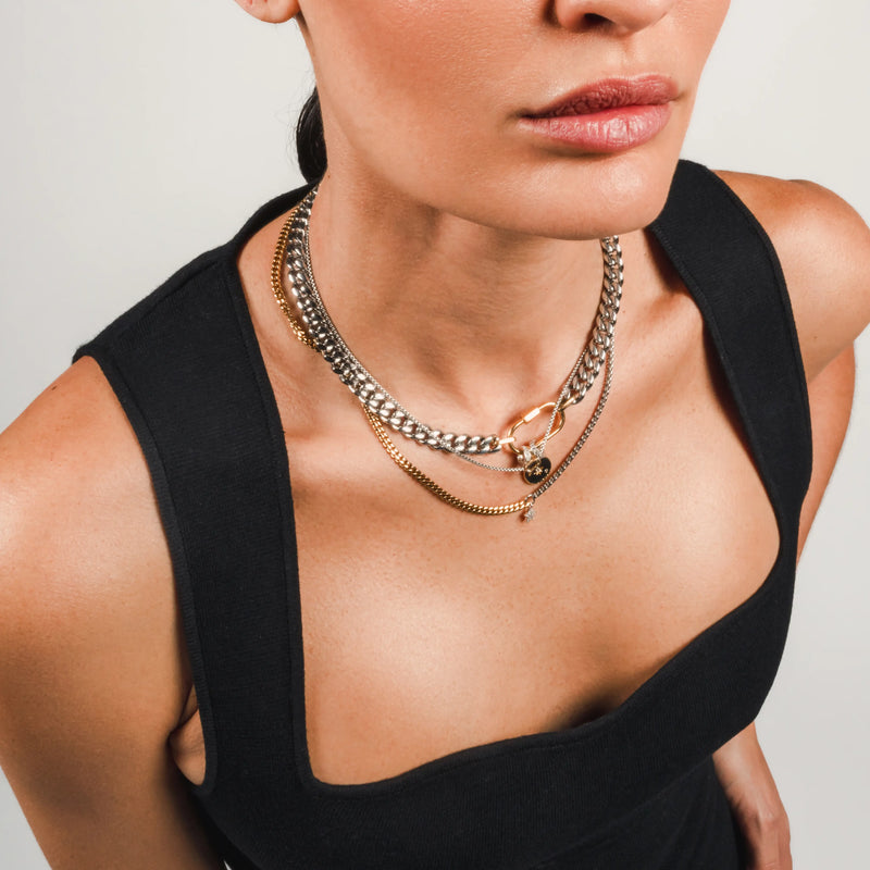 The Sleek Carabiner Cosmic Layered Necklace Set, which is a 3-piece mixed metal necklace set featuring silver and gold chains, a gold carabiner clasp, and celestial-themed charms for a striking, layered style.