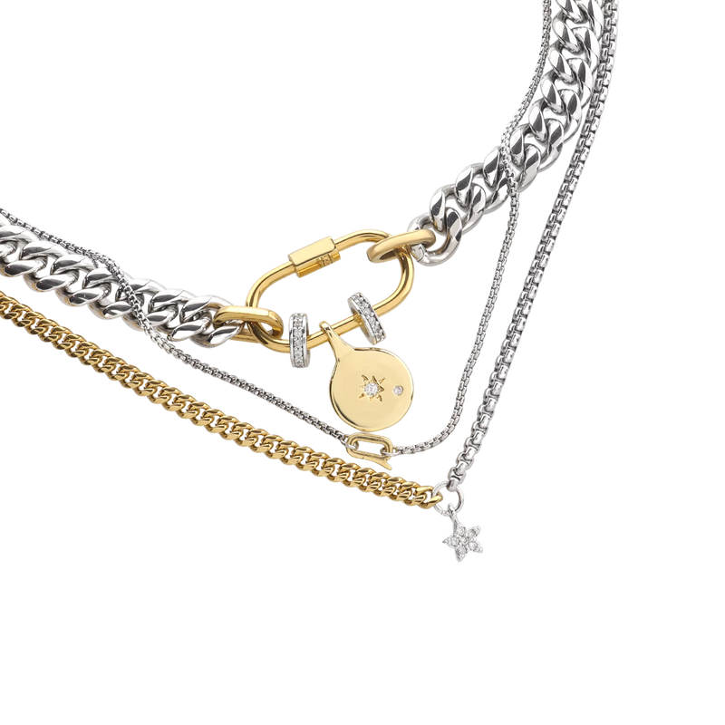 The Sleek Carabiner Cosmic Layered Necklace Set, which is a 3-piece mixed metal necklace set featuring thick silver and gold chains, a gold carabiner clasp, and celestial charms including a star pendant and a round charm with pavé accents for a layered cosmic look.