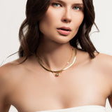 Model wearing the You and the Snake Layered Necklace, which is a set of 2 layered gold necklaces featuring a sleek snake chain, a delicate chain with geometric accents, and a fine chain with a small engraved pendant.