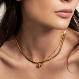 Model wearing the You and the Snake Layered Necklace, which is a set of 2 layered gold necklaces featuring a sleek snake chain, a delicate chain with geometric accents, and a fine chain with a small engraved pendant.
