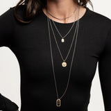 Model wearing The Charm Layered Necklace Set featuring four gold and silver-toned chains with distinct dangling charms in varied lengths.