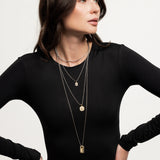 Model wearing The Charm Layered Necklace Set featuring four gold and silver-toned chains with distinct dangling charms in varied lengths.