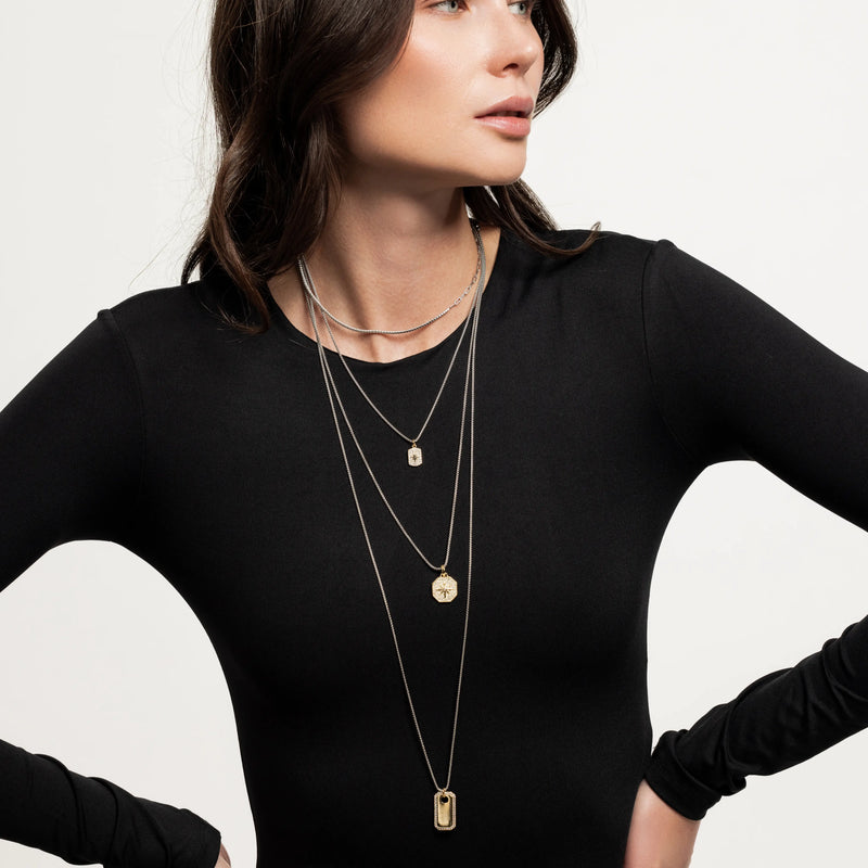Model wearing The Charm Layered Necklace Set featuring four gold and silver-toned chains with distinct dangling charms in varied lengths.