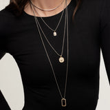Model wearing The Charm Layered Necklace Set featuring four gold and silver-toned chains with distinct dangling charms in varied lengths.