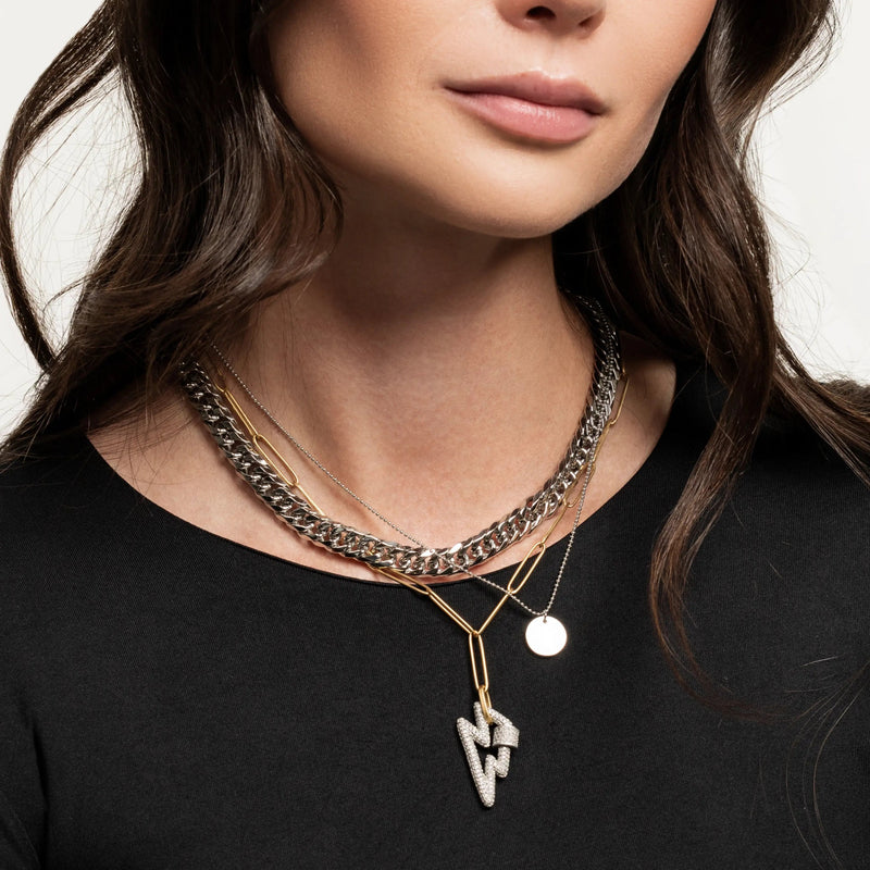 The Lightning layered necklace set, which is a three-piece layered necklace featuring a combination of silver and gold tones. It includes a chunky silver chain, a gold chain with a minimalist disc pendant, and a third chain with a striking lightning bolt pendant, creating a bold and dynamic look.