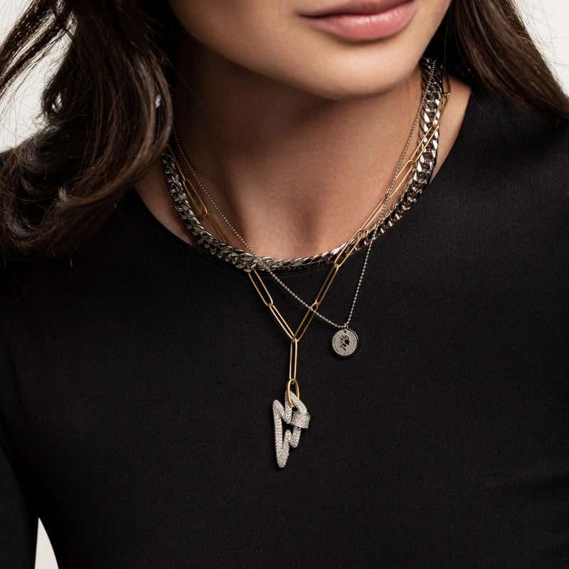 The Lightning layered necklace set, which is a three-piece layered necklace featuring a combination of silver and gold tones. It includes a chunky silver chain, a gold chain with a minimalist disc pendant, and a third chain with a striking lightning bolt pendant, creating a bold and dynamic look.