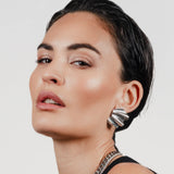 The WAVES OF SILVER EARRINGS, One piece, silver metal, bold shell-shaped earrings worn by model. Simple, elegant design with textured finish.